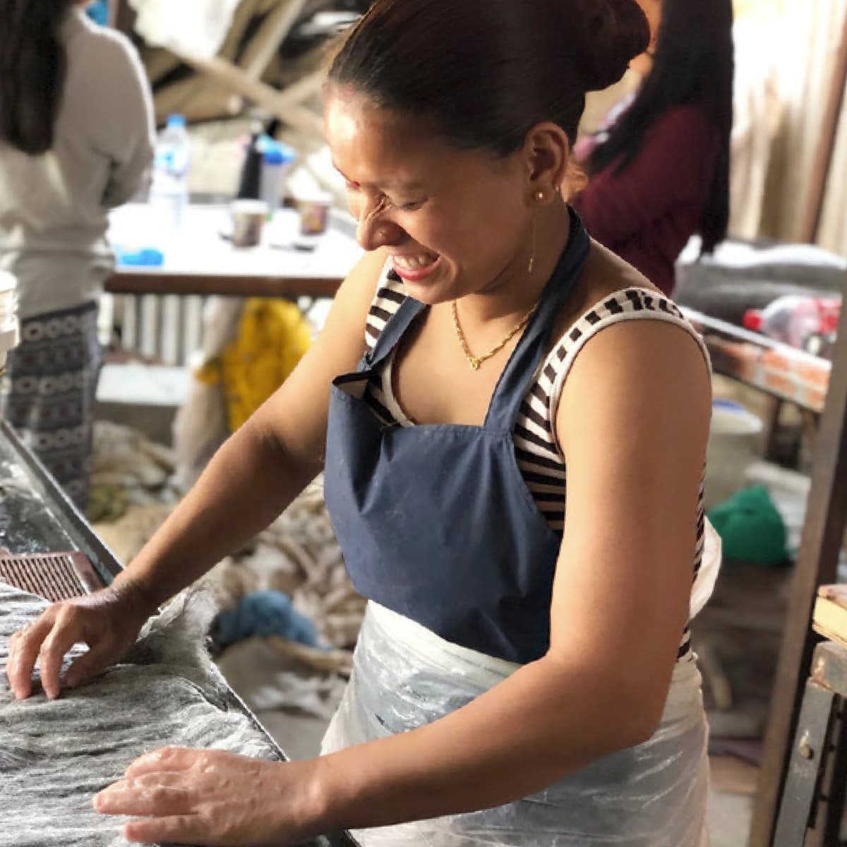 Nepal Woman in apron working with fabric, smiling.