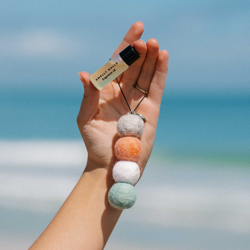 Hand holding colorful seapink balls and fragrance oil by the ocean.