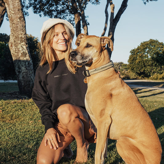 A woman smiling and kneeling beside a dog.
